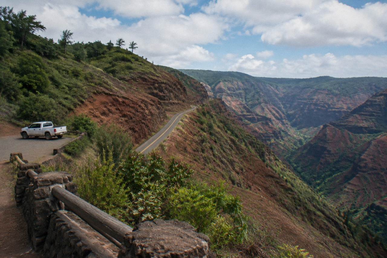 A scenic mountain road winding up red canyon cliffs with green ridges under scattered clouds