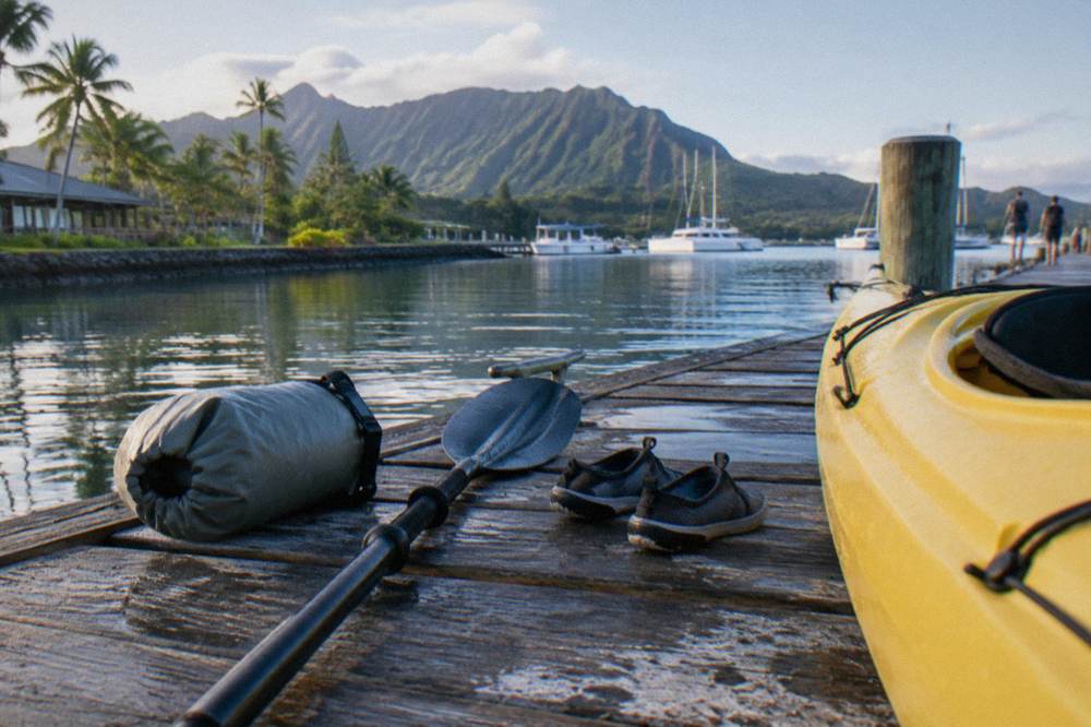 A dry bag, paddle and water shoes arranged on a dock beside a kayak
