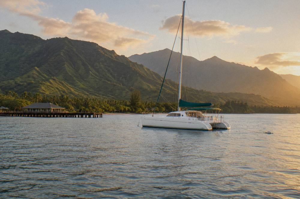A catamaran anchored in clear water beside tall green cliffs on the Na Pali coast