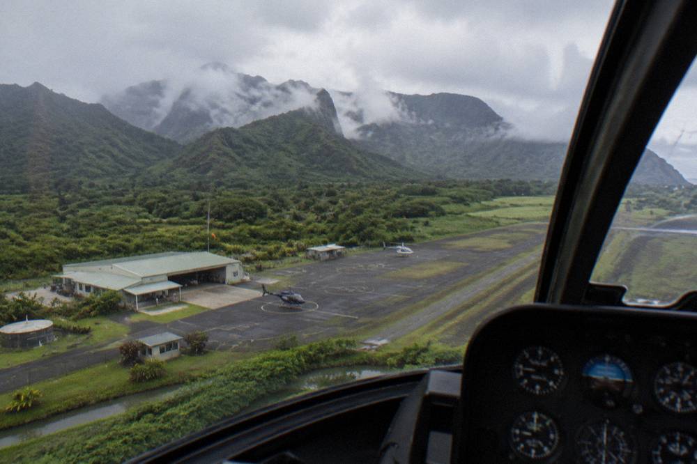 A helicopter cockpit view over clouds clinging to mountain ridges