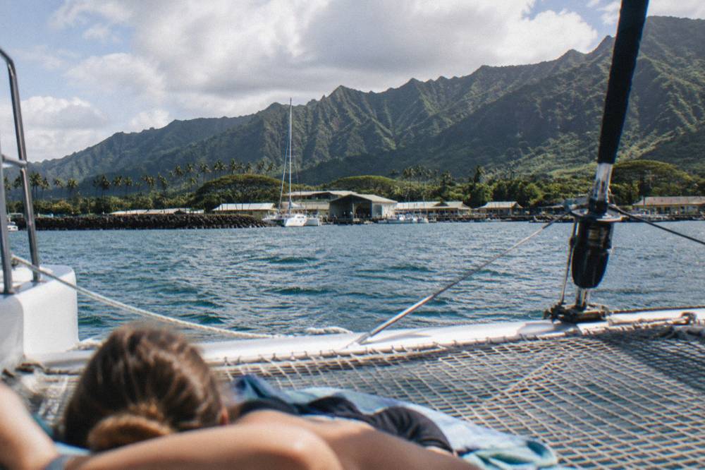 Passenger seating along the net of a catamaran with green cliffs in the distance