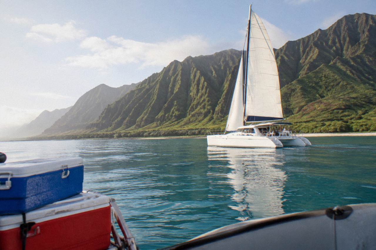 Catamaran cruising along the green sea cliffs of the Na Pali coast under morning light