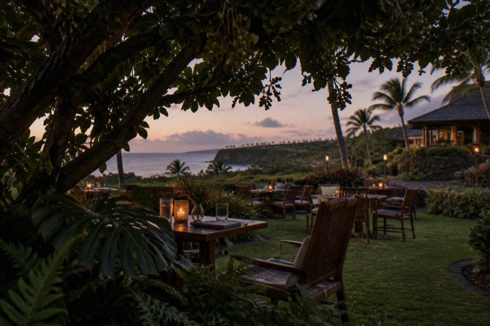 Garden tables set for an outdoor dinner among tropical foliage at dusk