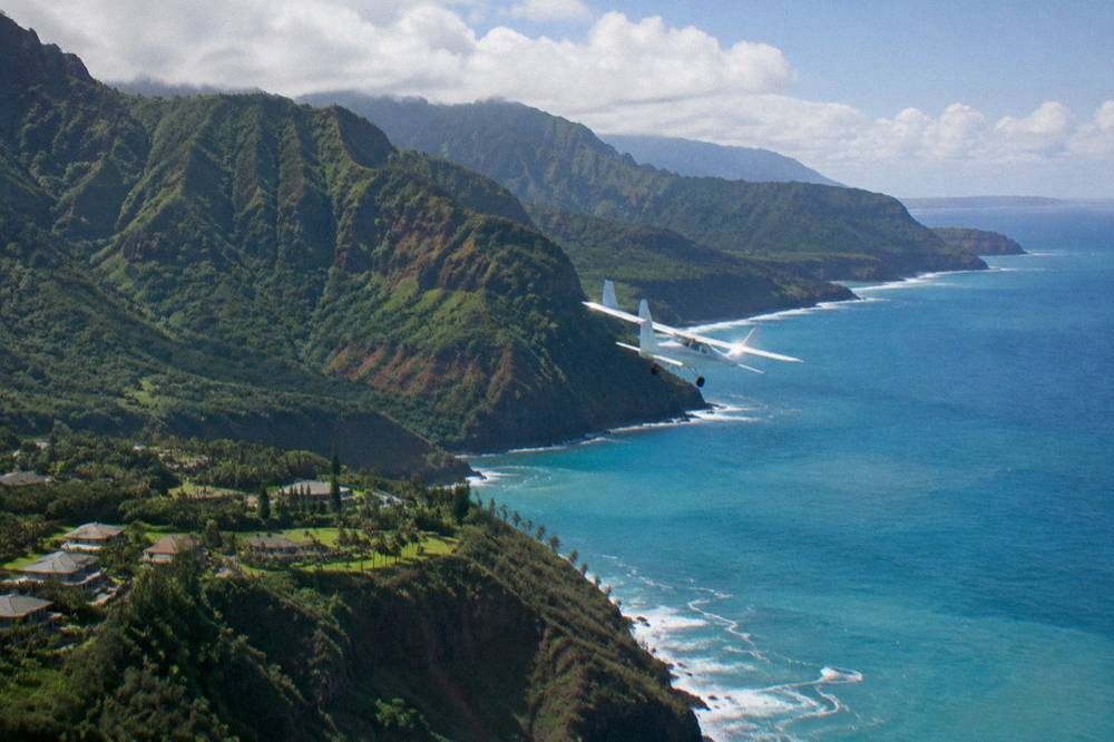 A small airplane flying along jagged sea cliffs on Kauai's northwest coast