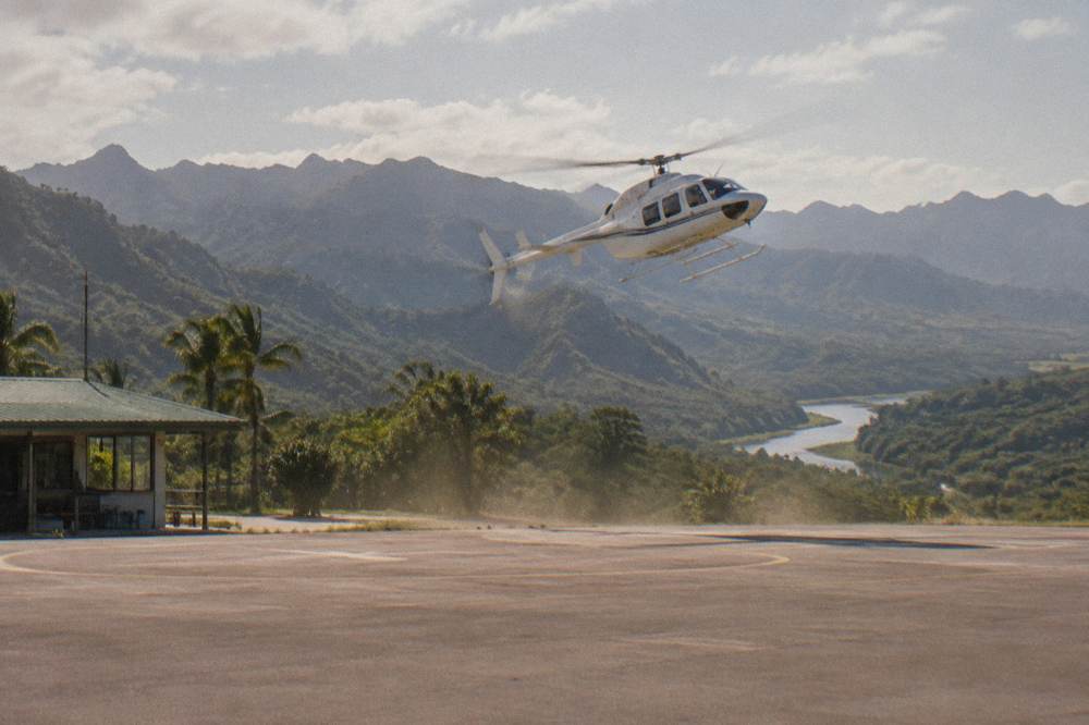 A helicopter flying above layered jungle ridges above a winding river valley