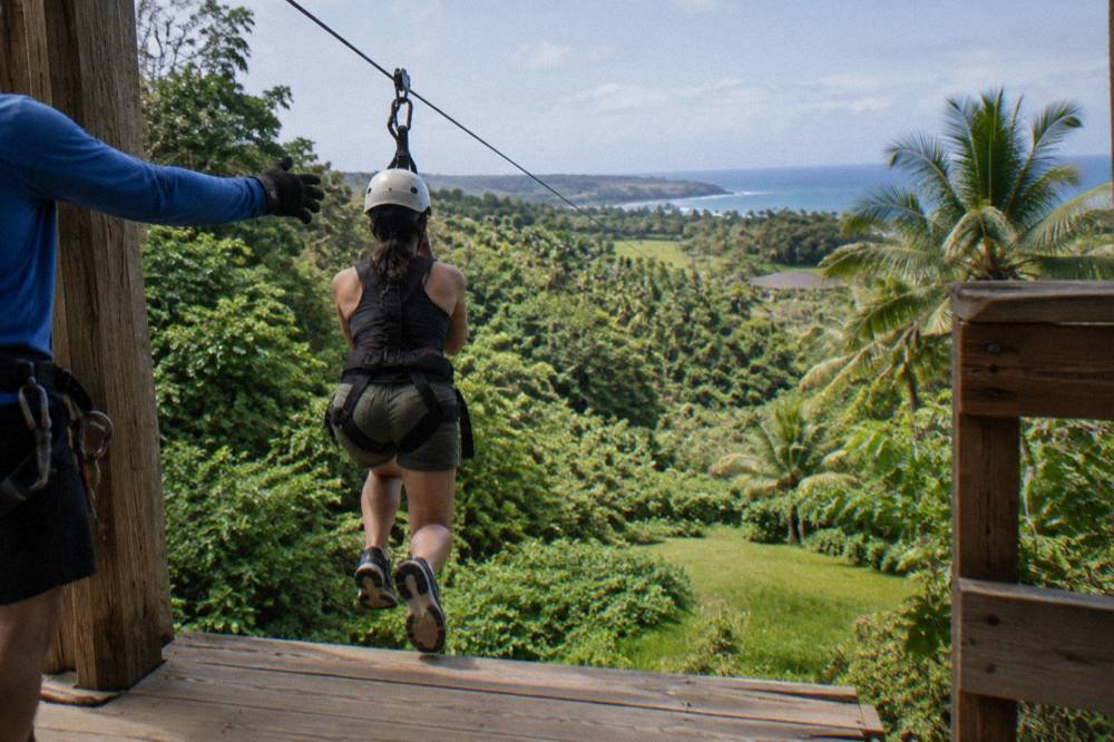 A rider in a harness stepping off a wooden zipline platform into treetops