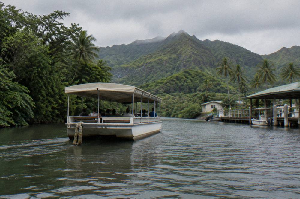 A flat-bottom riverboat cruising between dense green jungle walls on a wide calm river