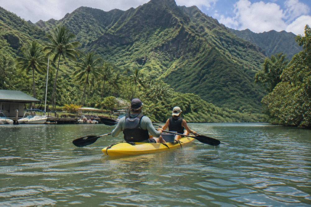 A kayak floating on a wide green river with tall fern-covered valley walls