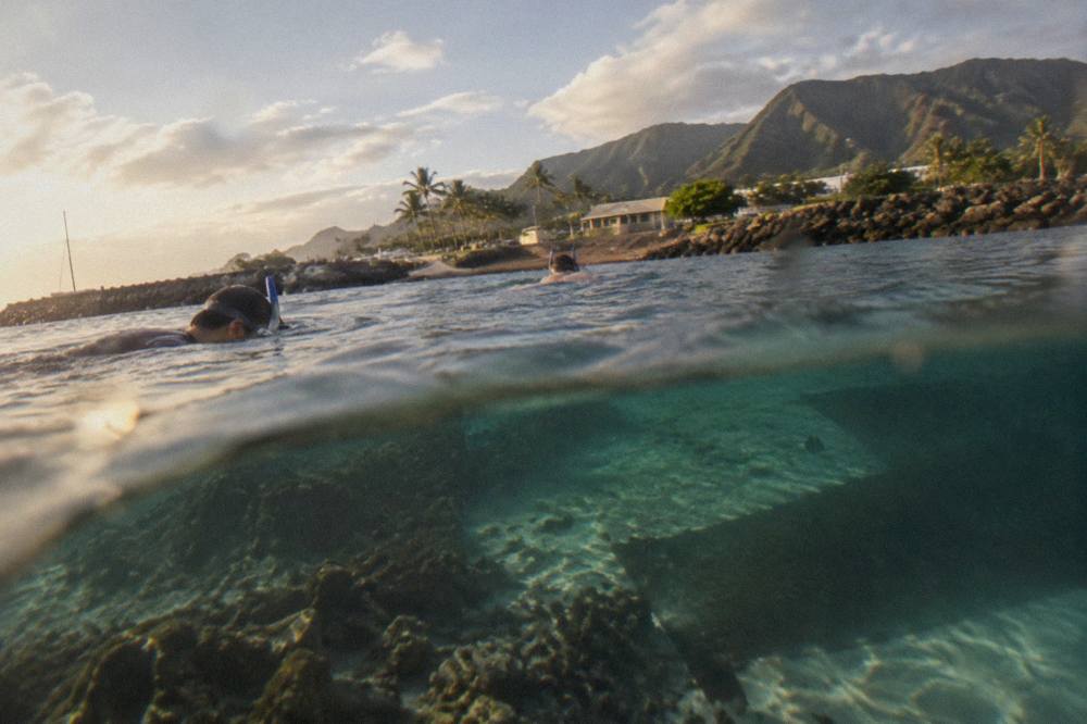 Snorkelers floating over a coral reef in clear turquoise water near a rocky Kauai shoreline