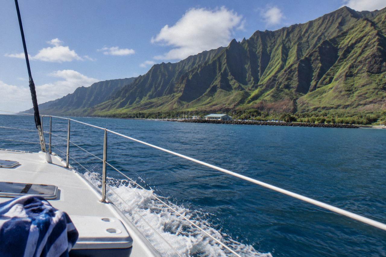 A catamaran cruising along the green sea cliffs of the Na Pali coast at midday