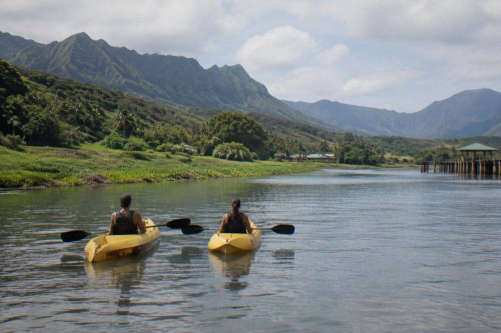 Two kayaks floating on a wide calm river between steep green valley walls
