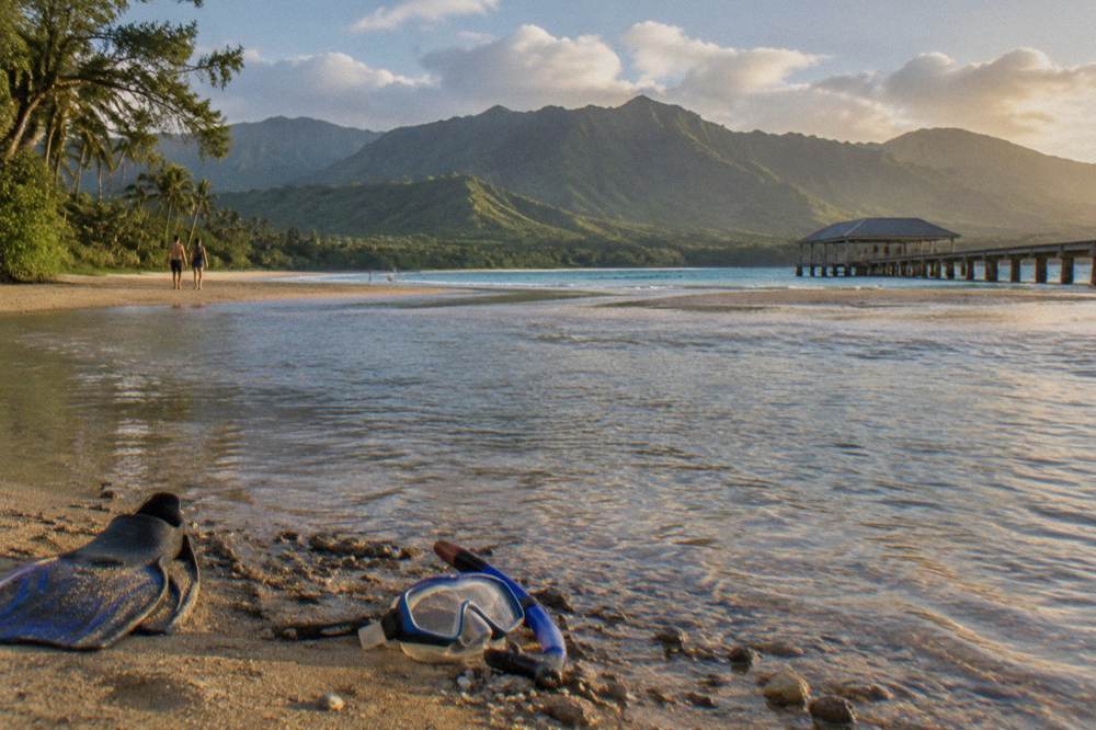 A wide river mouth opening toward a turquoise bay with green mountains behind