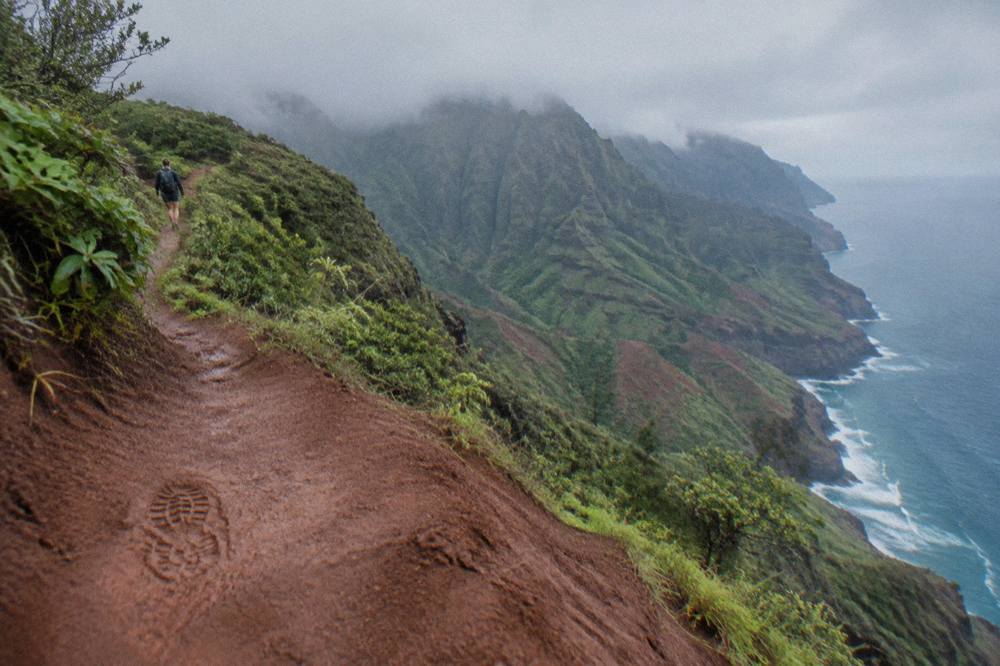 A narrow dirt trail carved into a steep green cliff above a turquoise ocean
