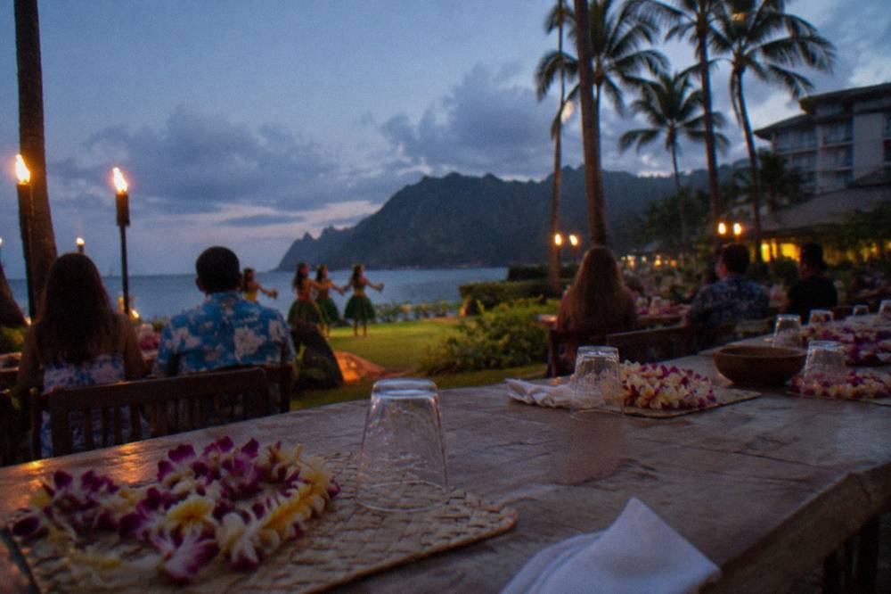 Guest table set for an outdoor luau dinner with tropical flowers and tiki torches