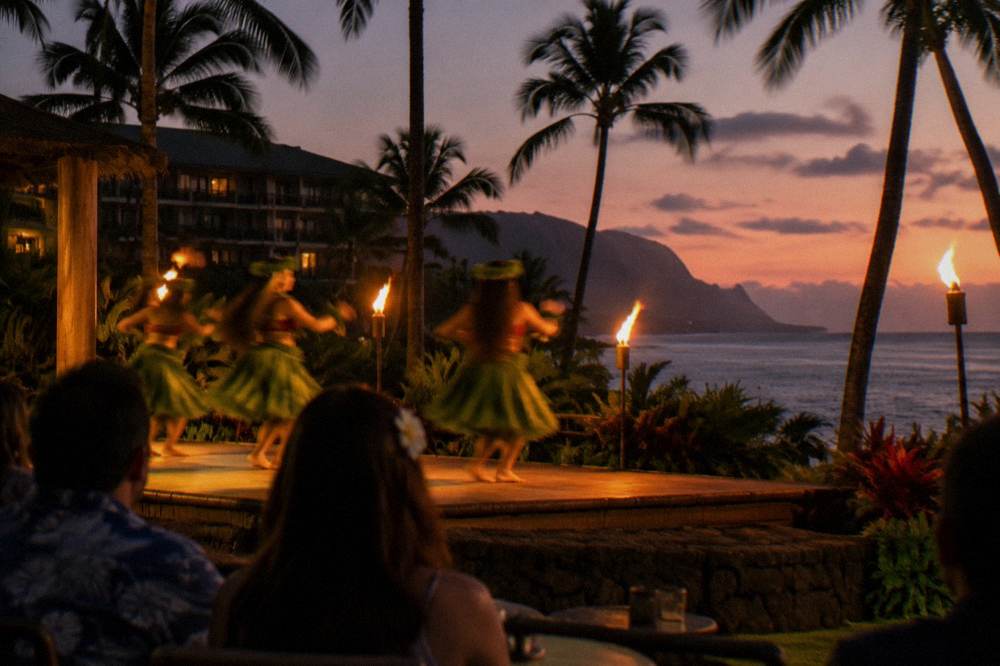 Hula dancers performing on an outdoor luau stage at dusk