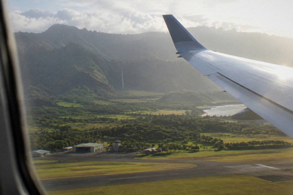 A small airplane wing above green Kauai valleys and a distant waterfall