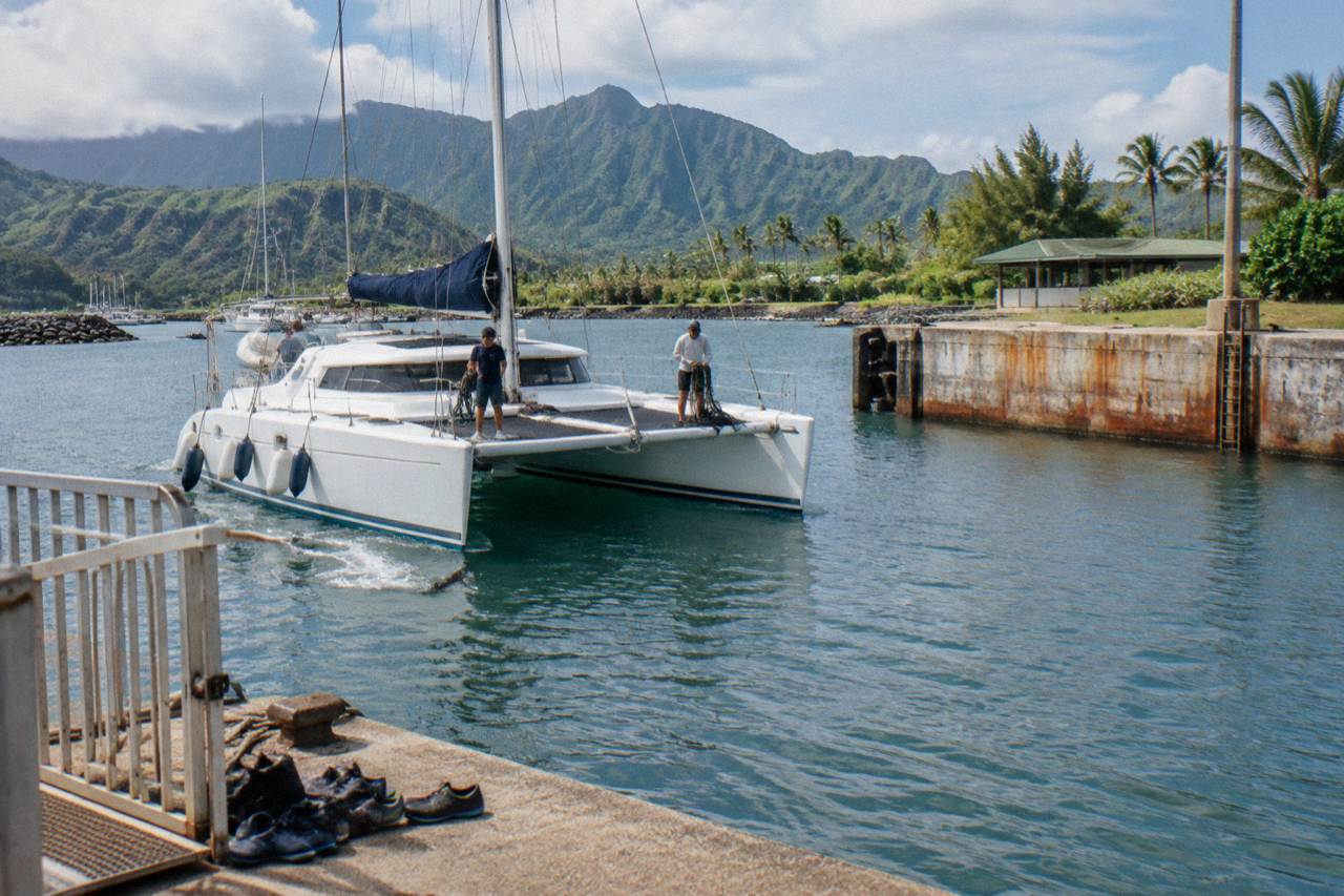 A catamaran cruising along the green sea cliffs of the Na Pali Coast under a bright sky