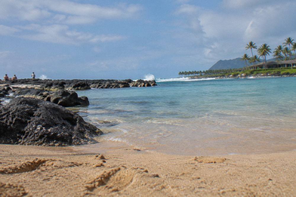 Wide crescent bay with golden sand, calm turquoise water and green mountain ridges behind