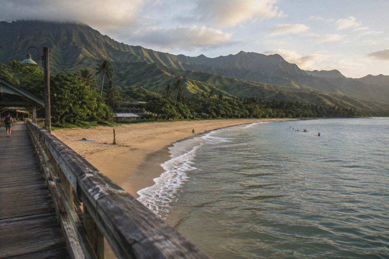 Curved golden sand beach backed by steep green cliffs along a tropical coastline