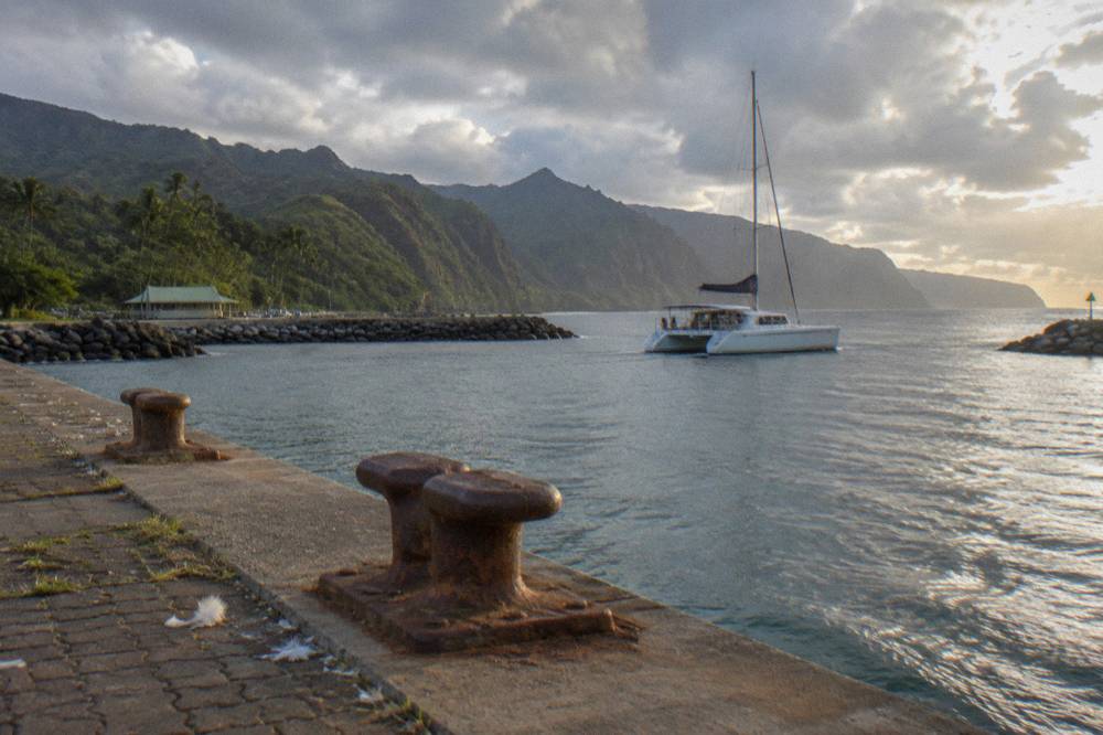 A catamaran cruising along green sea cliffs under a mix of sun and clouds