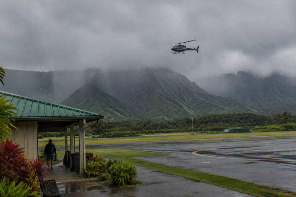 A helicopter flying past rain clouds above a green Kauai mountain ridge