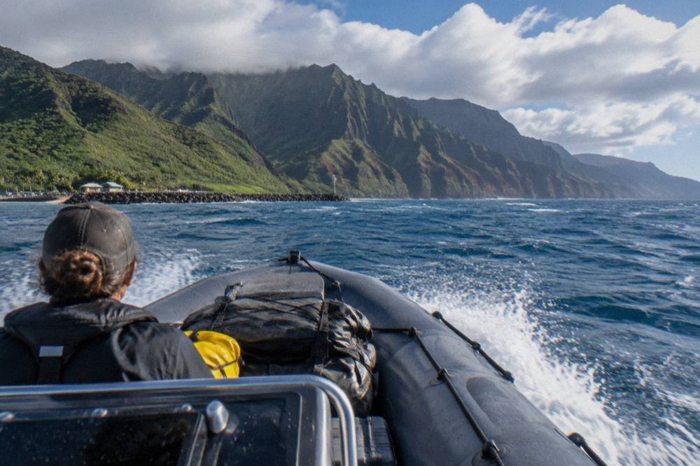 A rigid inflatable raft cutting across open water near the Na Pali cliffs with white spray at the bow