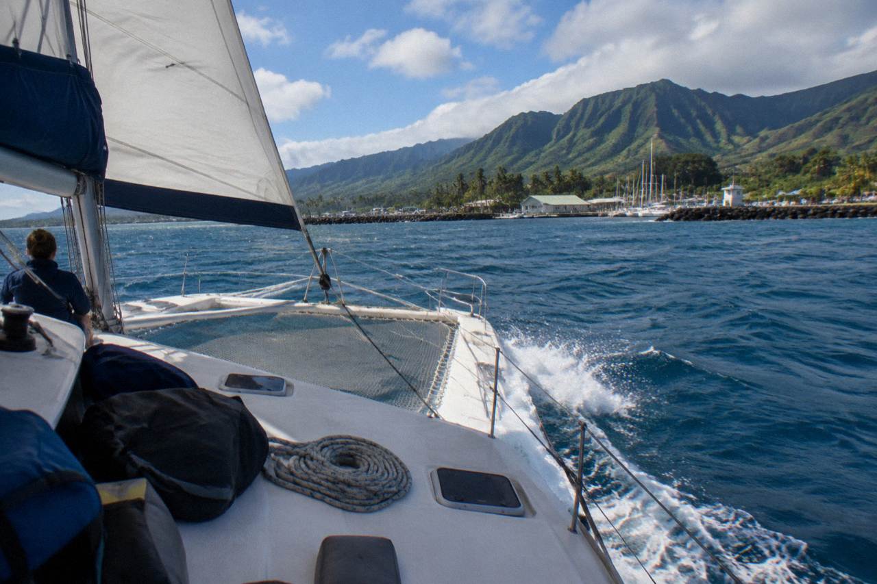 A catamaran underway along the sheer green cliffs of the Na Pali coast on open blue water