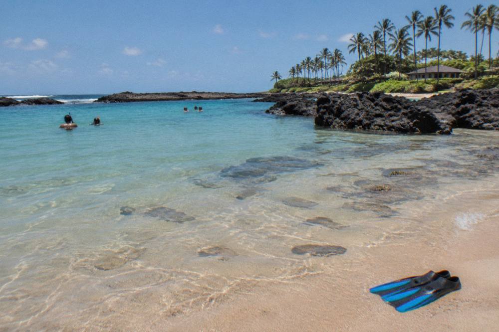 Calm turquoise lagoon over a shallow reef with dark lava rock framing the far edge.