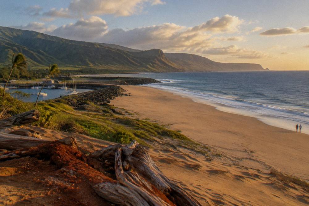 Wide empty beach backed by tall sand dunes with distant sea cliffs under scattered clouds.