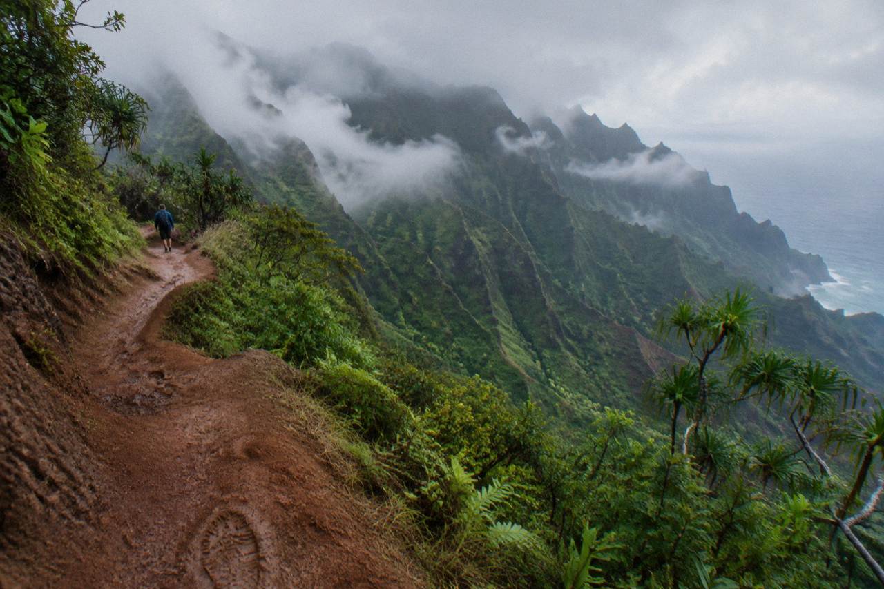 A green ridgeline trail winding above a deep jungle valley on Kauai