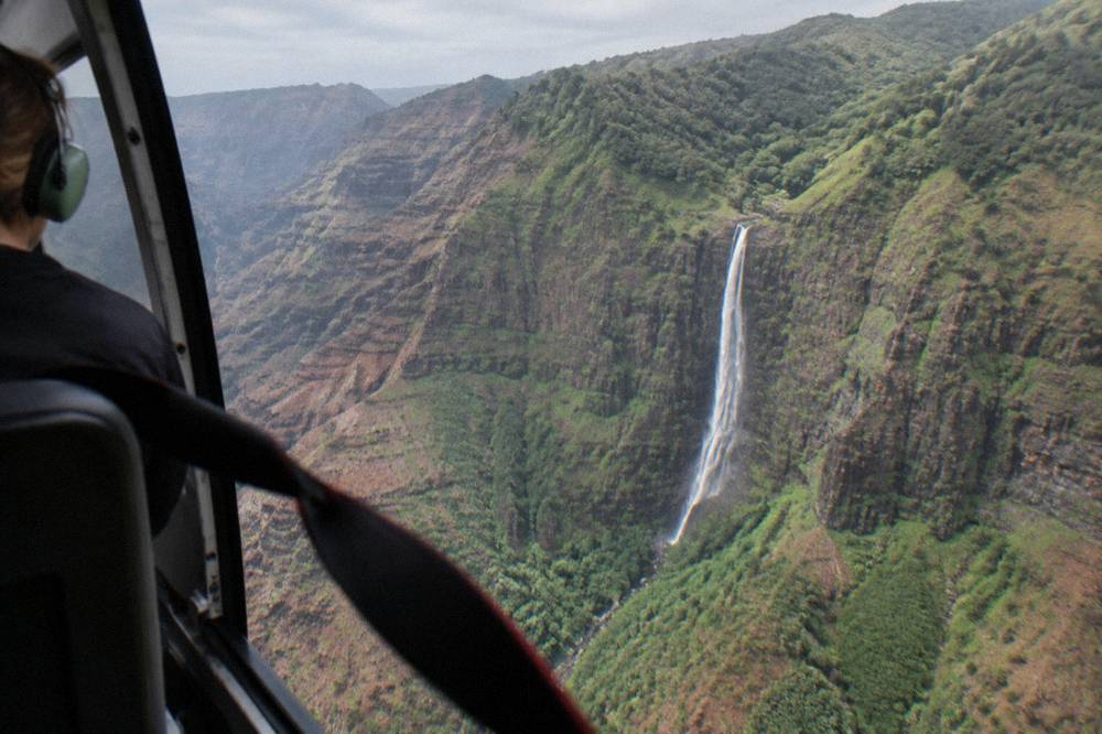 A waterfall pouring down a steep green cliff face seen from the air