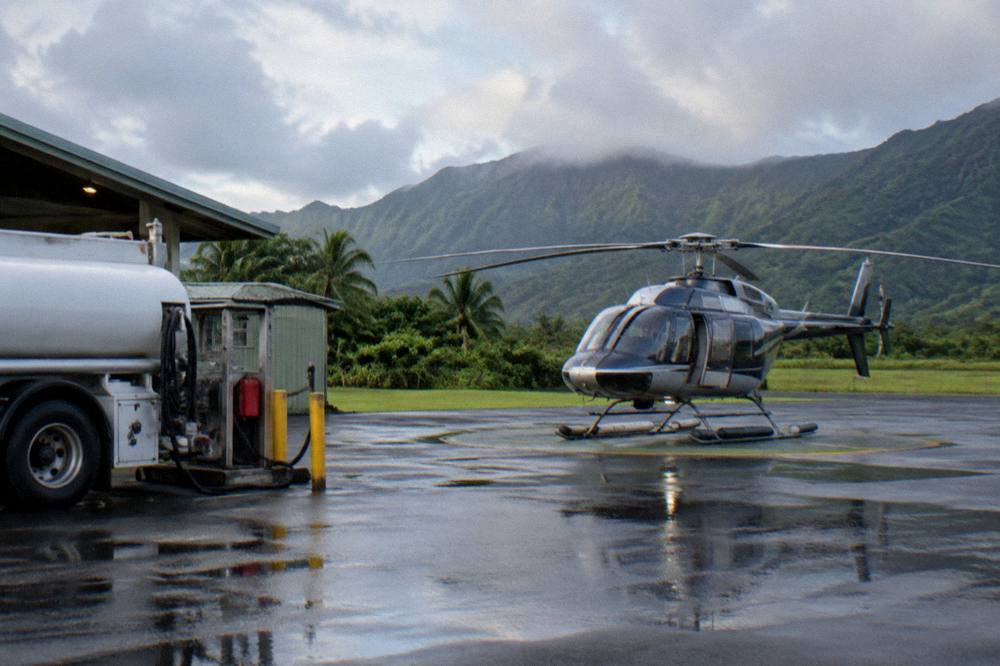 A helicopter on a paved pad at an airport with green hills behind