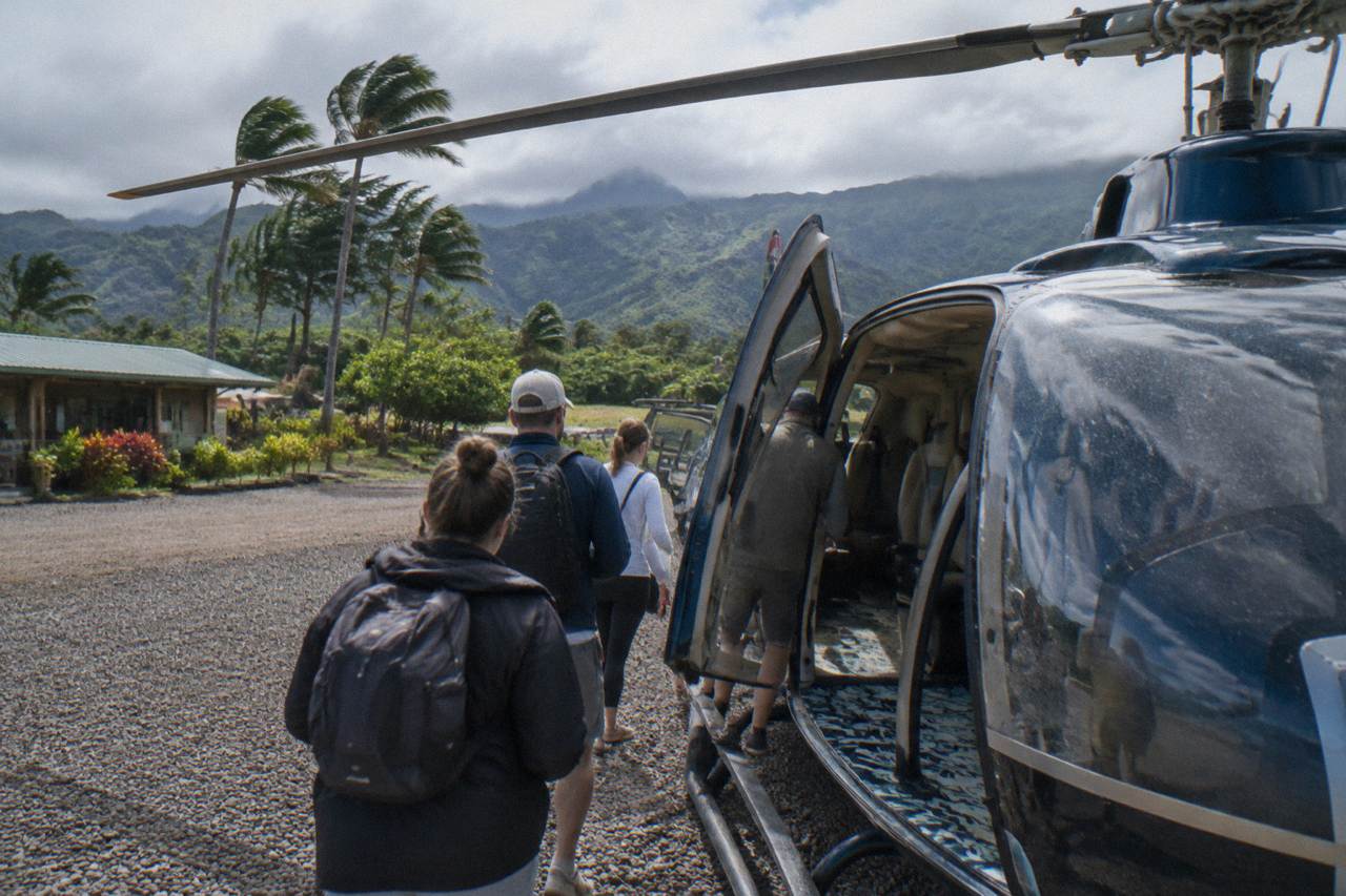A helicopter flying along a green cliff coastline with waterfalls dropping to the ocean