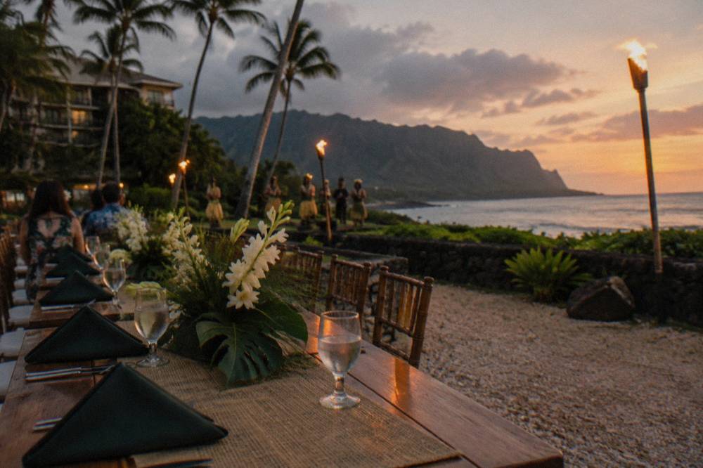 Long dinner table set with tropical flower centerpieces and folded napkins at dusk