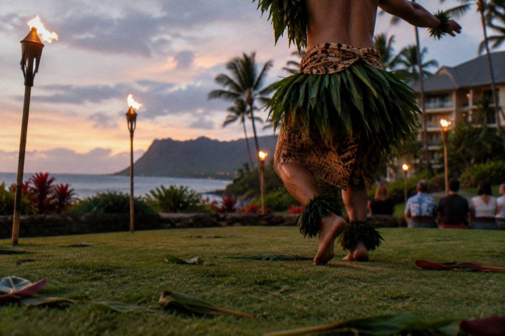 Performer in traditional attire dancing near burning torches as daylight fades
