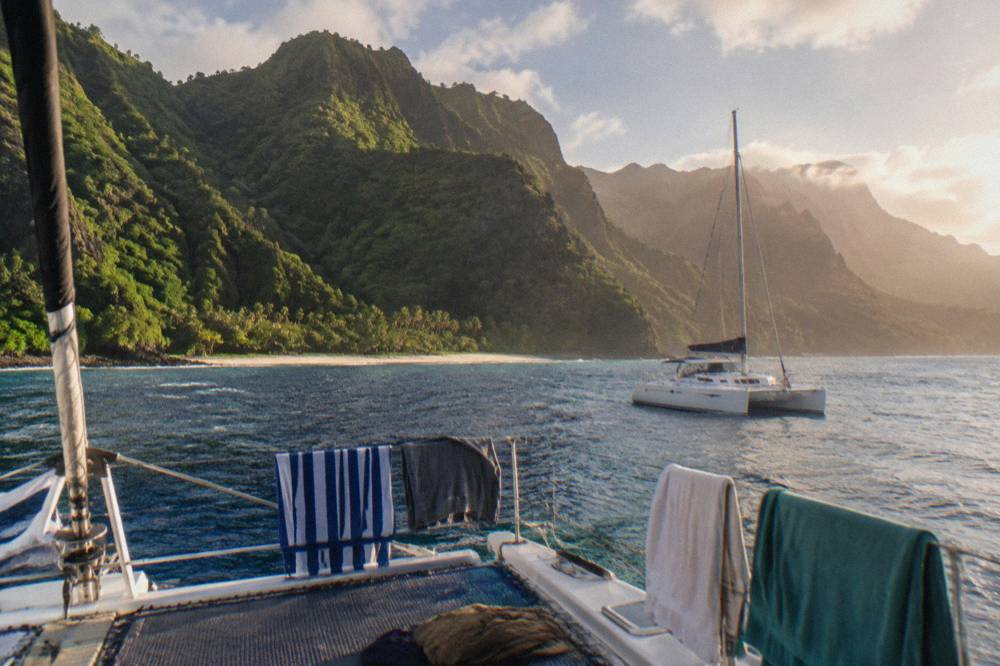 A catamaran anchored near steep green sea cliffs along a tropical coastline