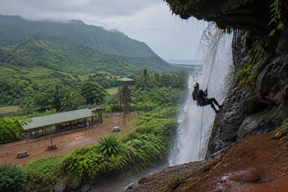 A roped descender lowering down a wet rock face beside falling water