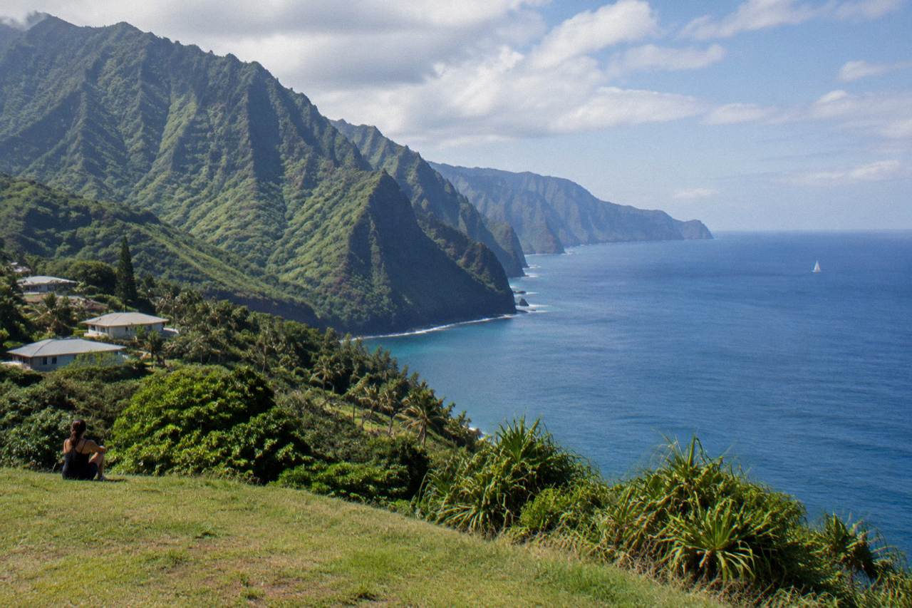 Green sea cliffs of the Na Pali coast rising above calm blue water under scattered clouds