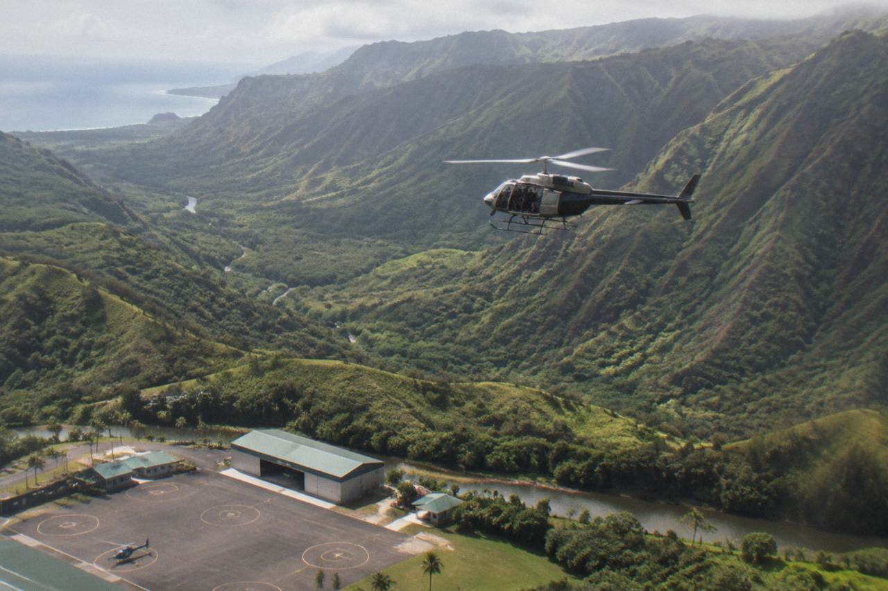 A small helicopter flying over green Kauai ridgelines above a deep valley