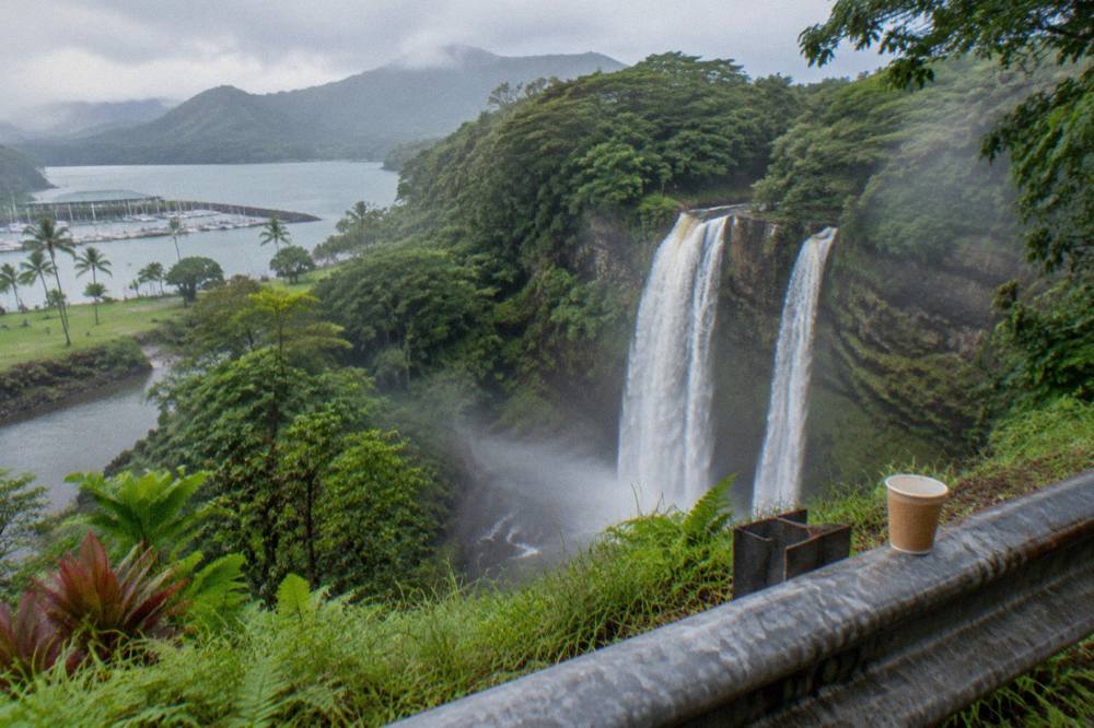 A roadside overlook with a view of a double waterfall plunging into a green valley