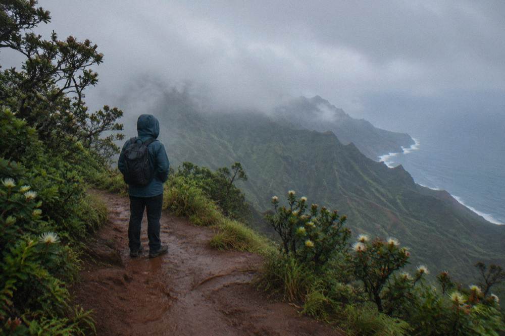 A hiker on a ridge trail looking down at a winding river and green valley
