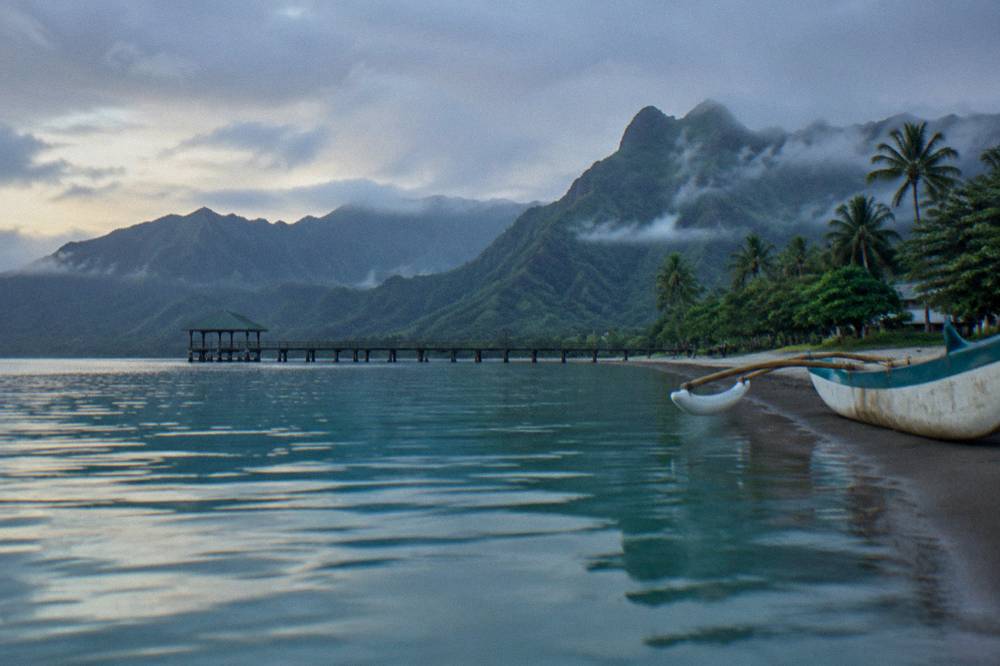 Calm turquoise bay water at sunrise with mist over green mountains