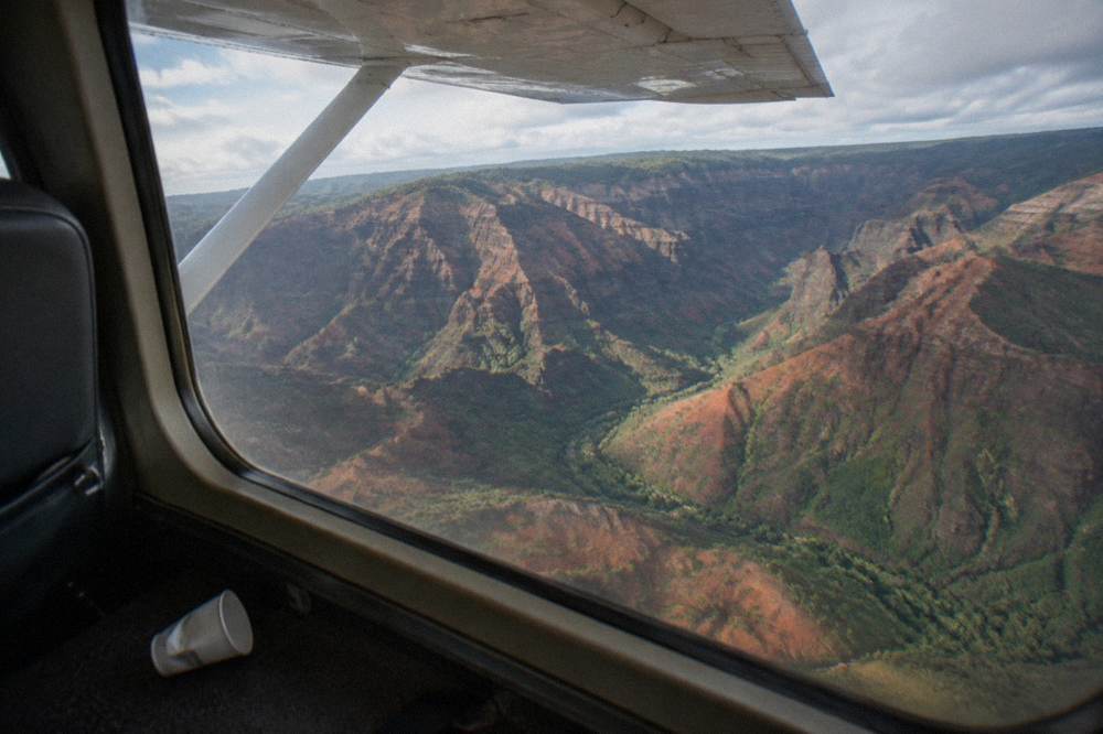 The view from an airplane window over red canyon walls and green ridges