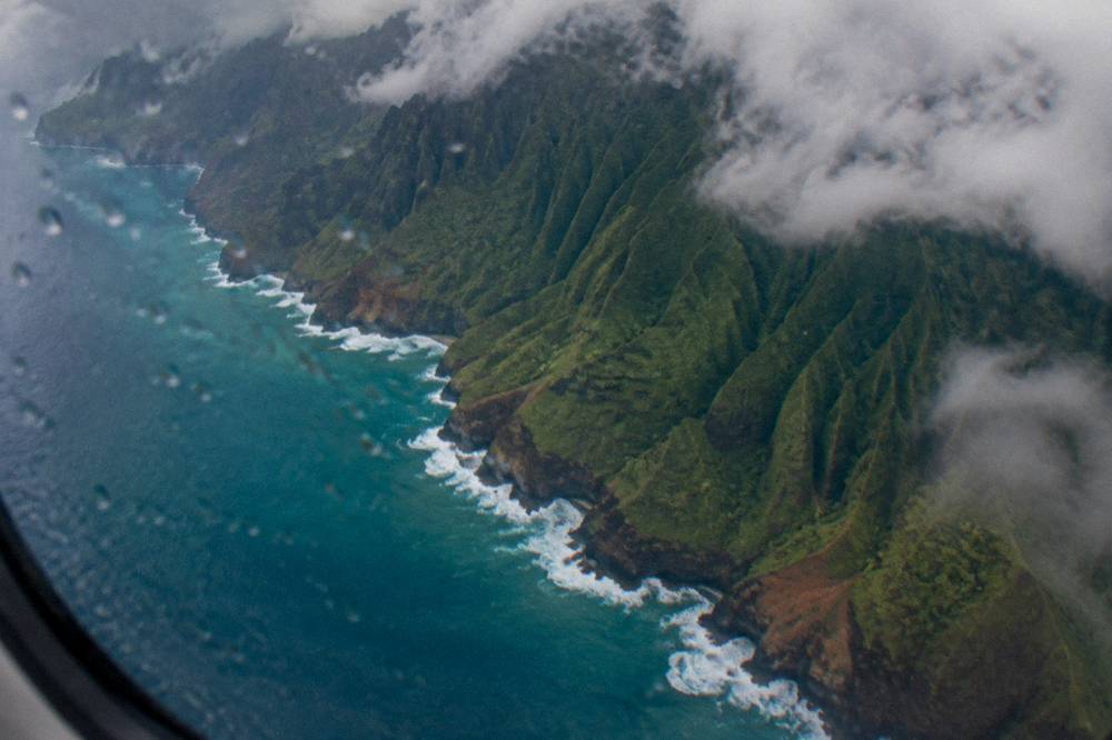 Steep emerald cliffs along a coastline seen from above with waves breaking at their base