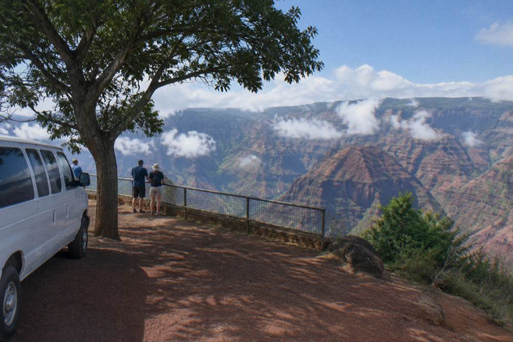 Tour van parked at a canyon overlook with layered red rock cliffs beyond