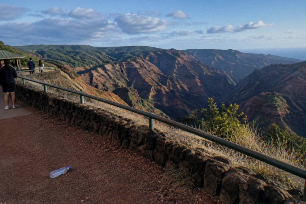 Deep red and green canyon walls under scattered clouds seen from a roadside overlook