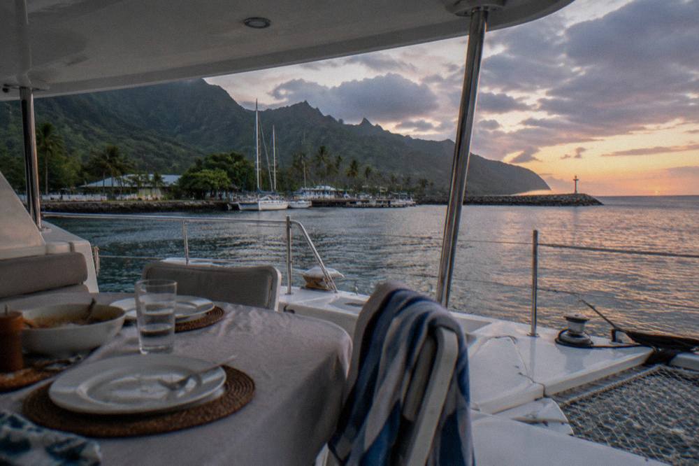 A covered dining table set on the deck of a catamaran with the ocean horizon behind it.