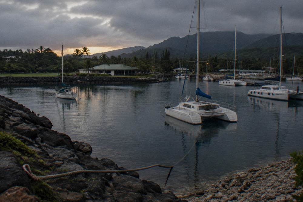 A small boat harbor at dusk with masts and the silhouette of hills behind.