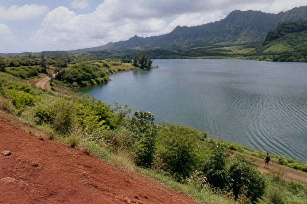 A reservoir ringed by green hills under scattered clouds, its surface lightly rippled