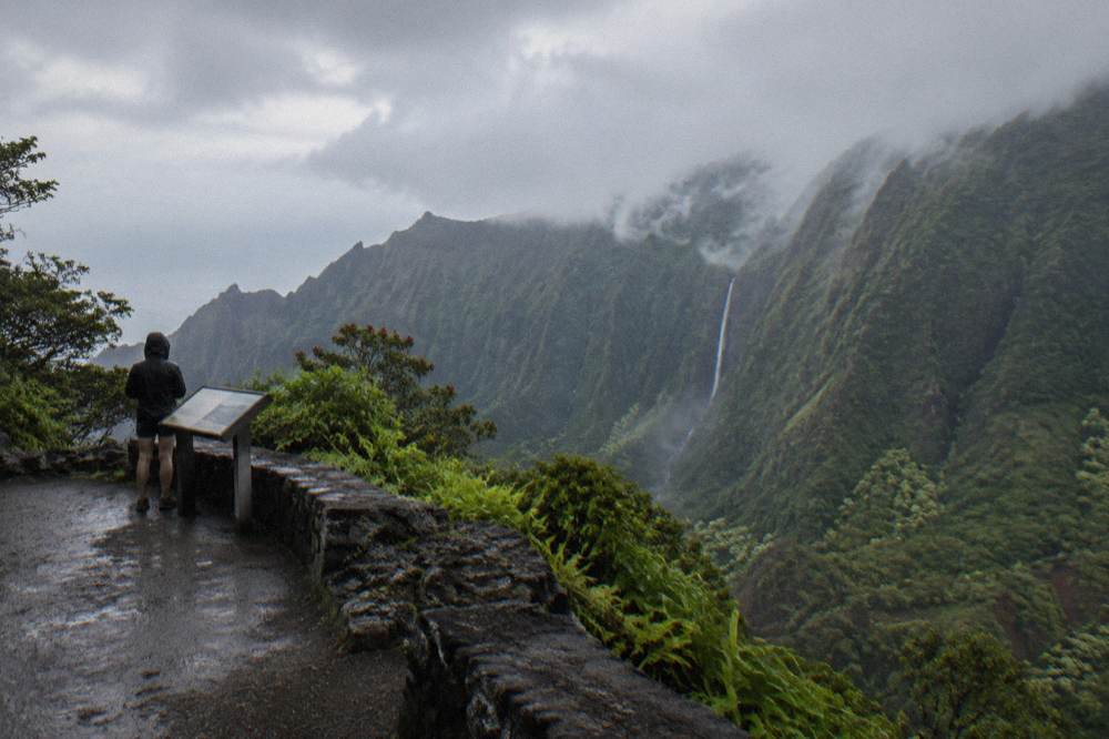 Low clouds spilling over a steep green Kauai valley with a thin waterfall dropping into mist.